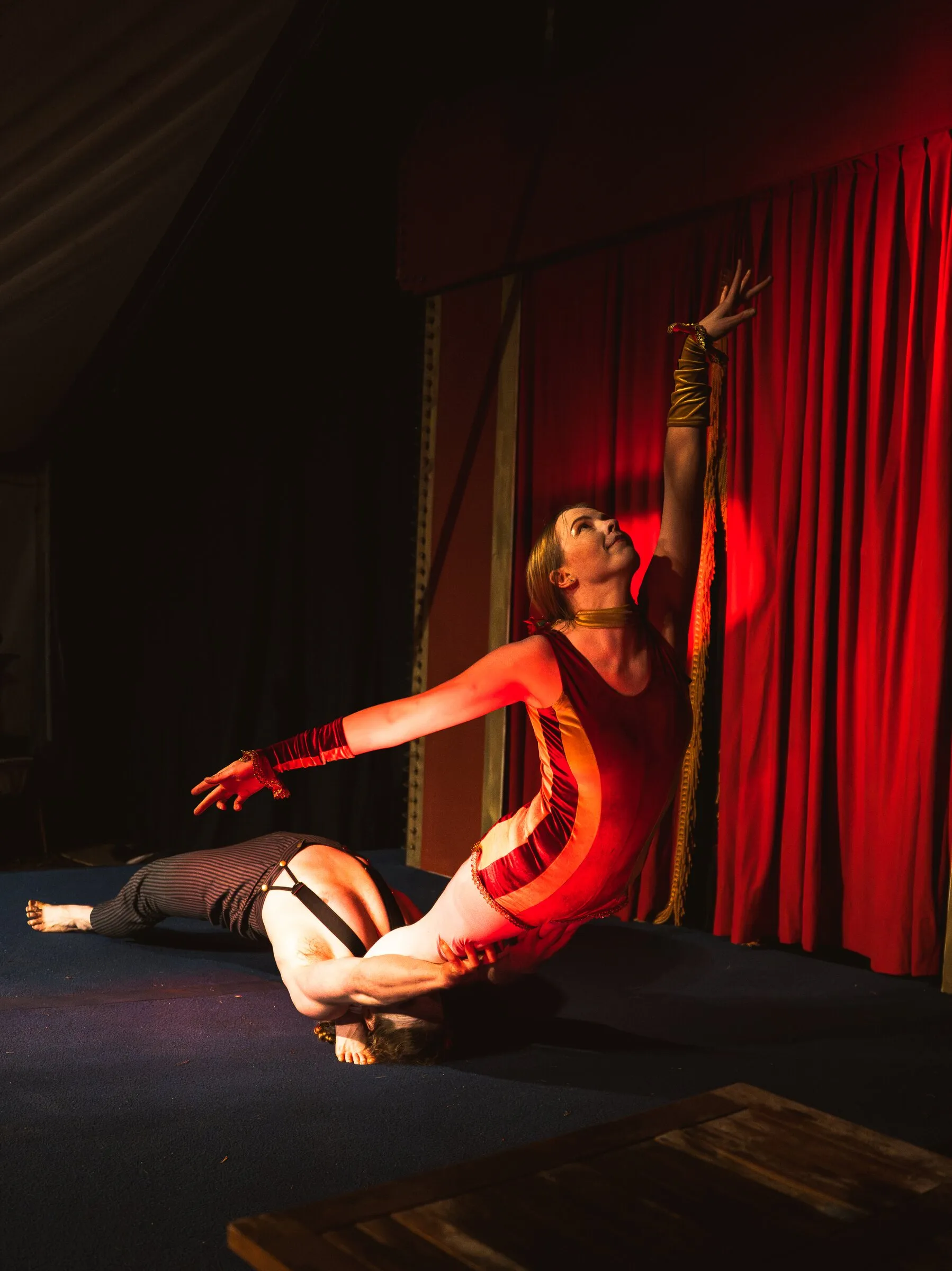 A Kuroneko Circus acrobat reaching skyward as her partner lies on the stage behind her