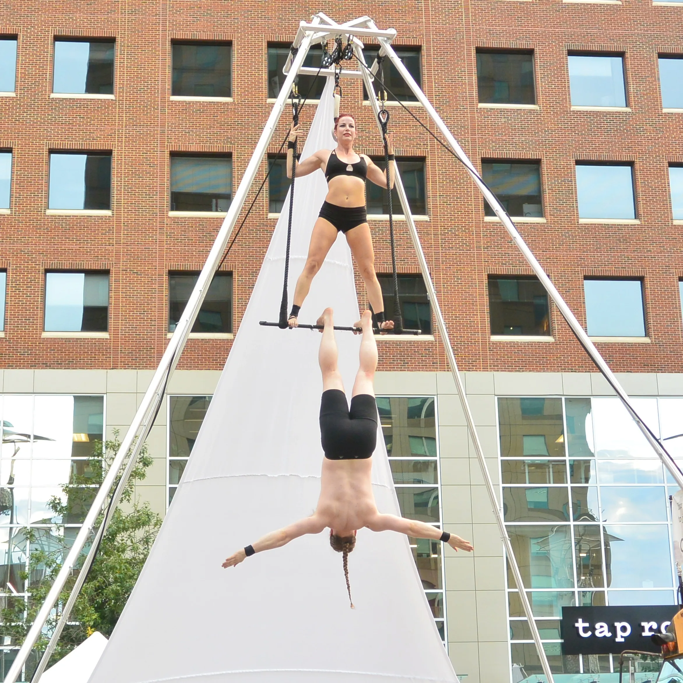 A Kuroneko Circus aerialist hanging inverted beneath her partner on an outdoor rig in North Carolina