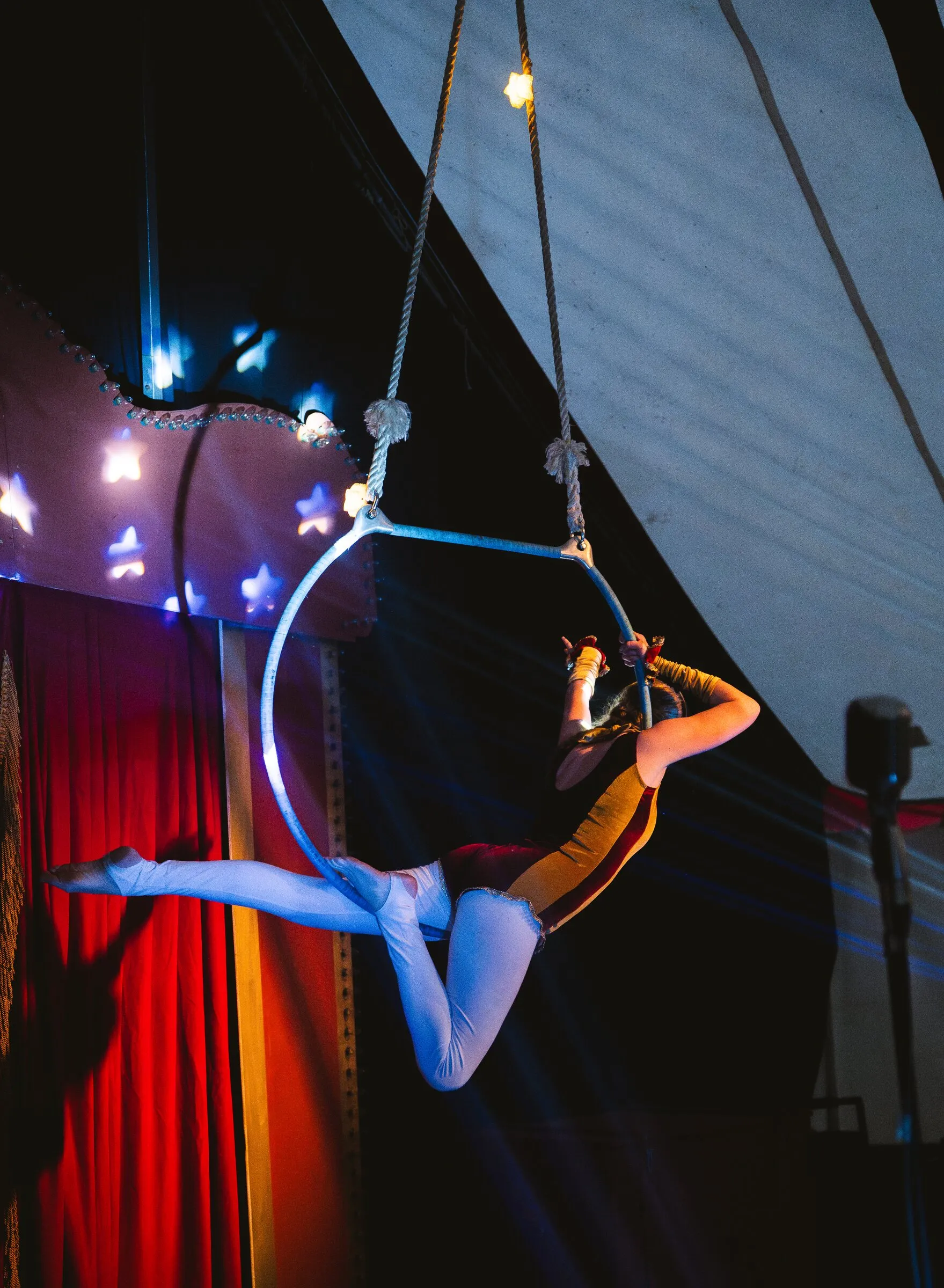 A Kuroneko Circus aerialist extending her legs from an aerial hoop against the canvas