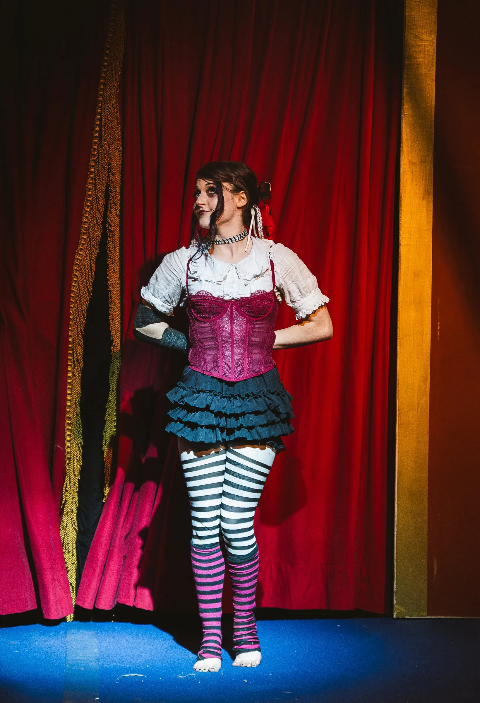 A Kuroneko Circus aerialist in a pink corset and striped stockings posing on stage before her act