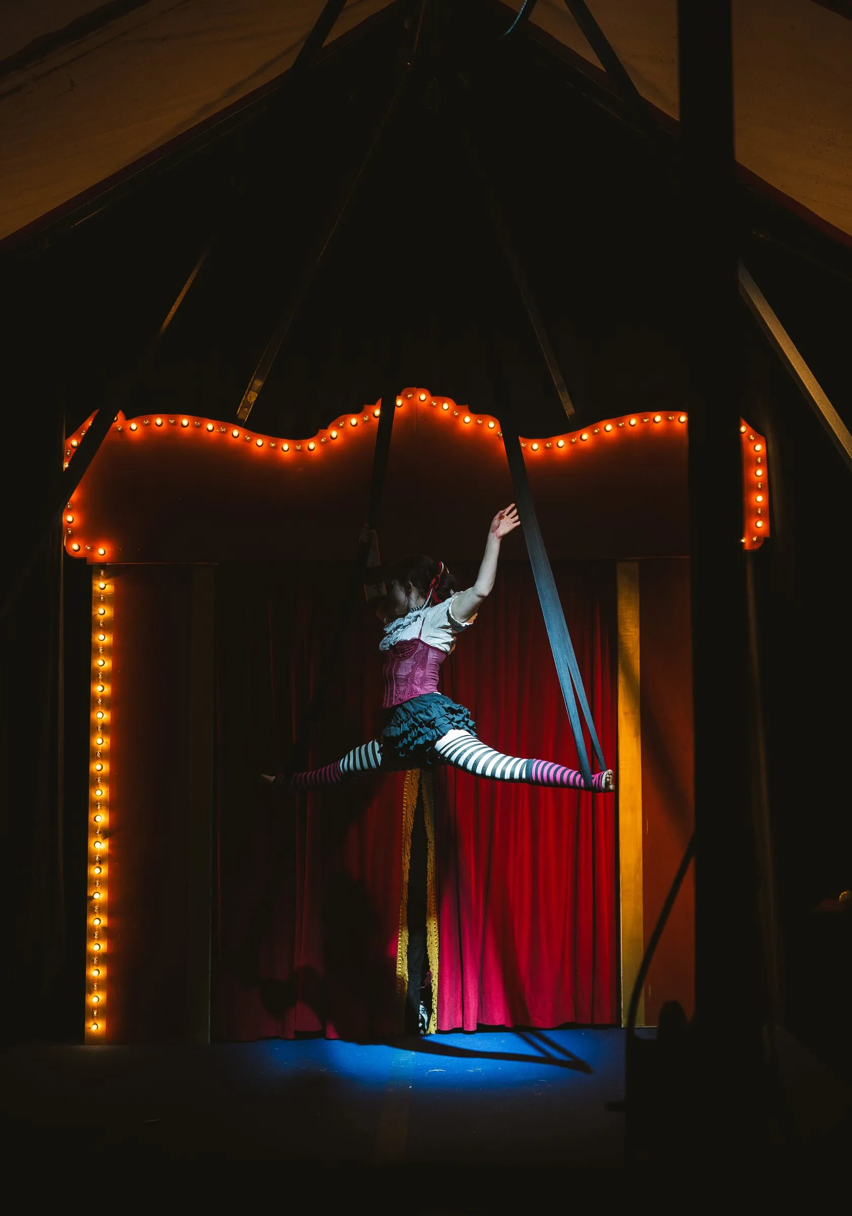A Kuroneko Circus aerialist holding a split in aerial loops beneath the big top canvas