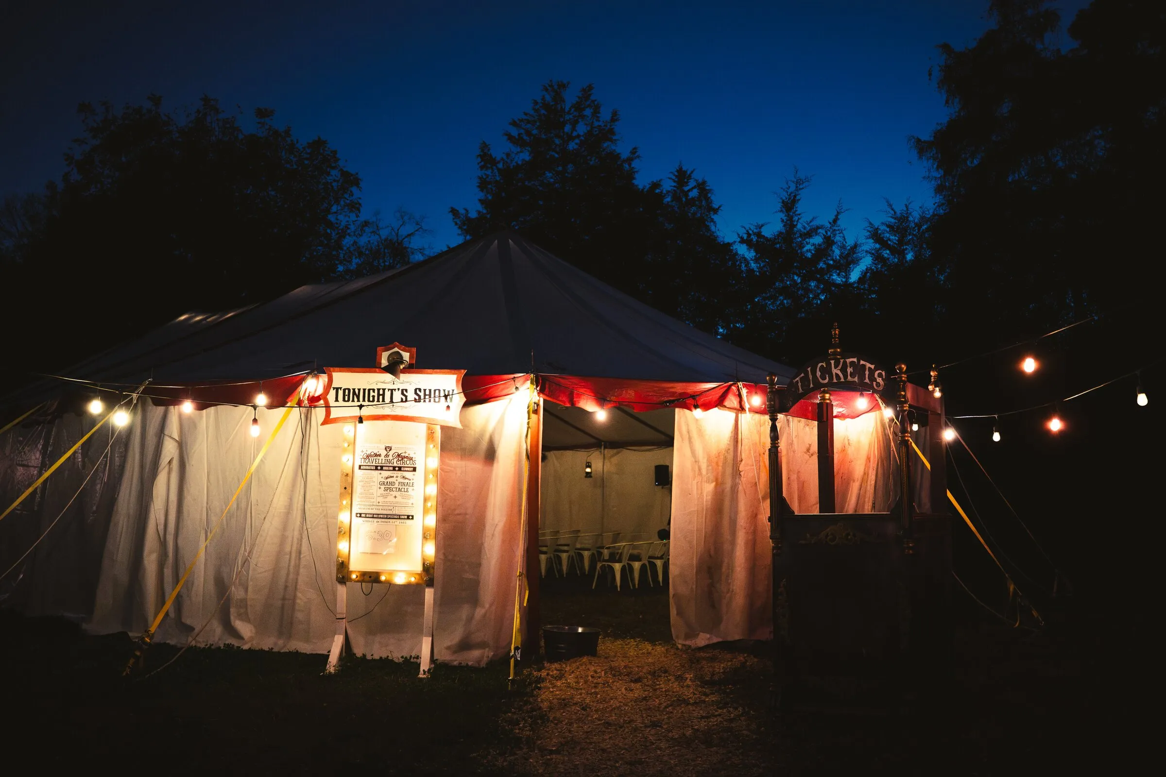 The Kuroneko Circus tent, show bill, and ticket booth glowing under string lights at dusk in North Carolina