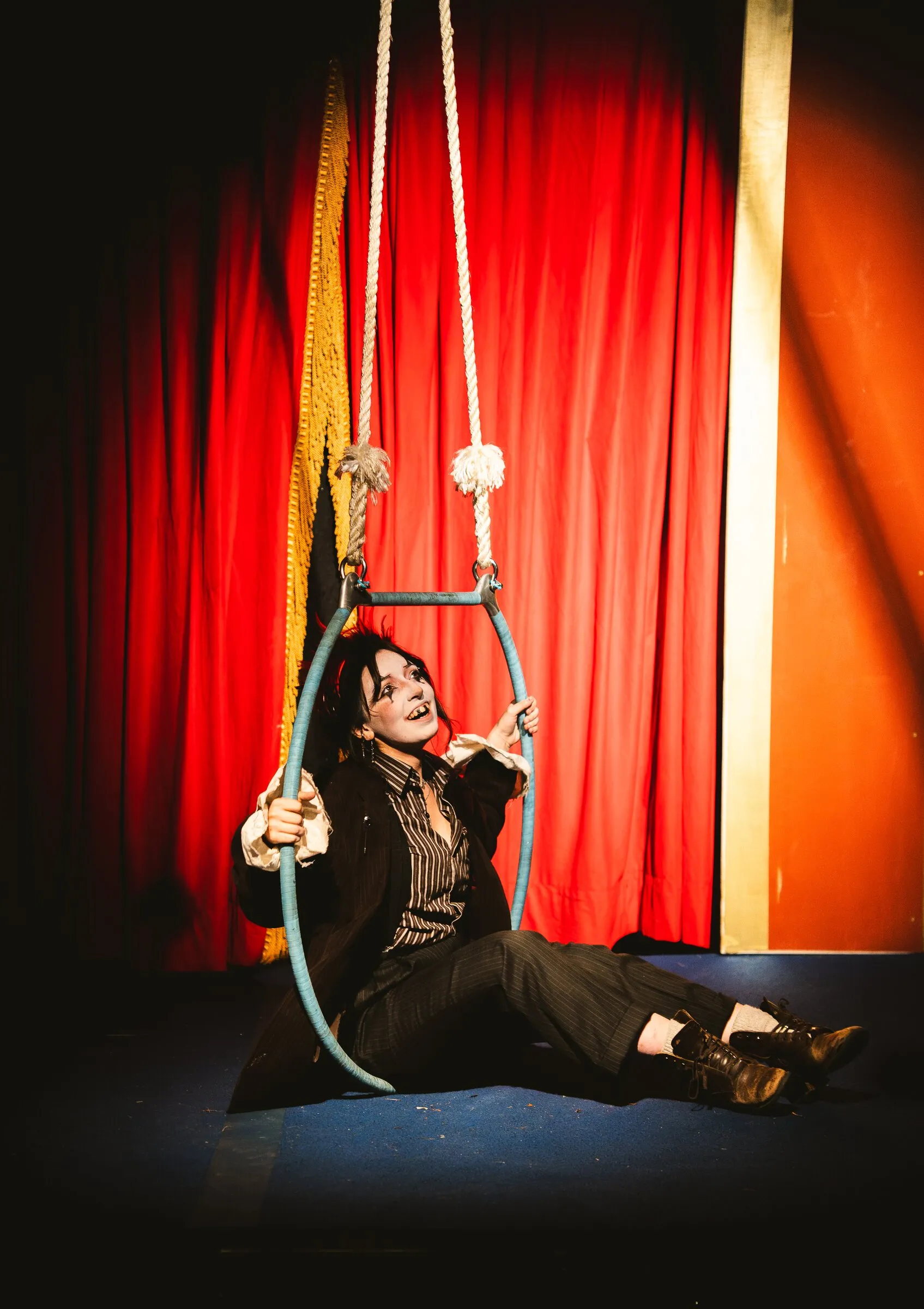 A Kuroneko Circus sideshow clown sitting on the stage inside a lowered aerial hoop