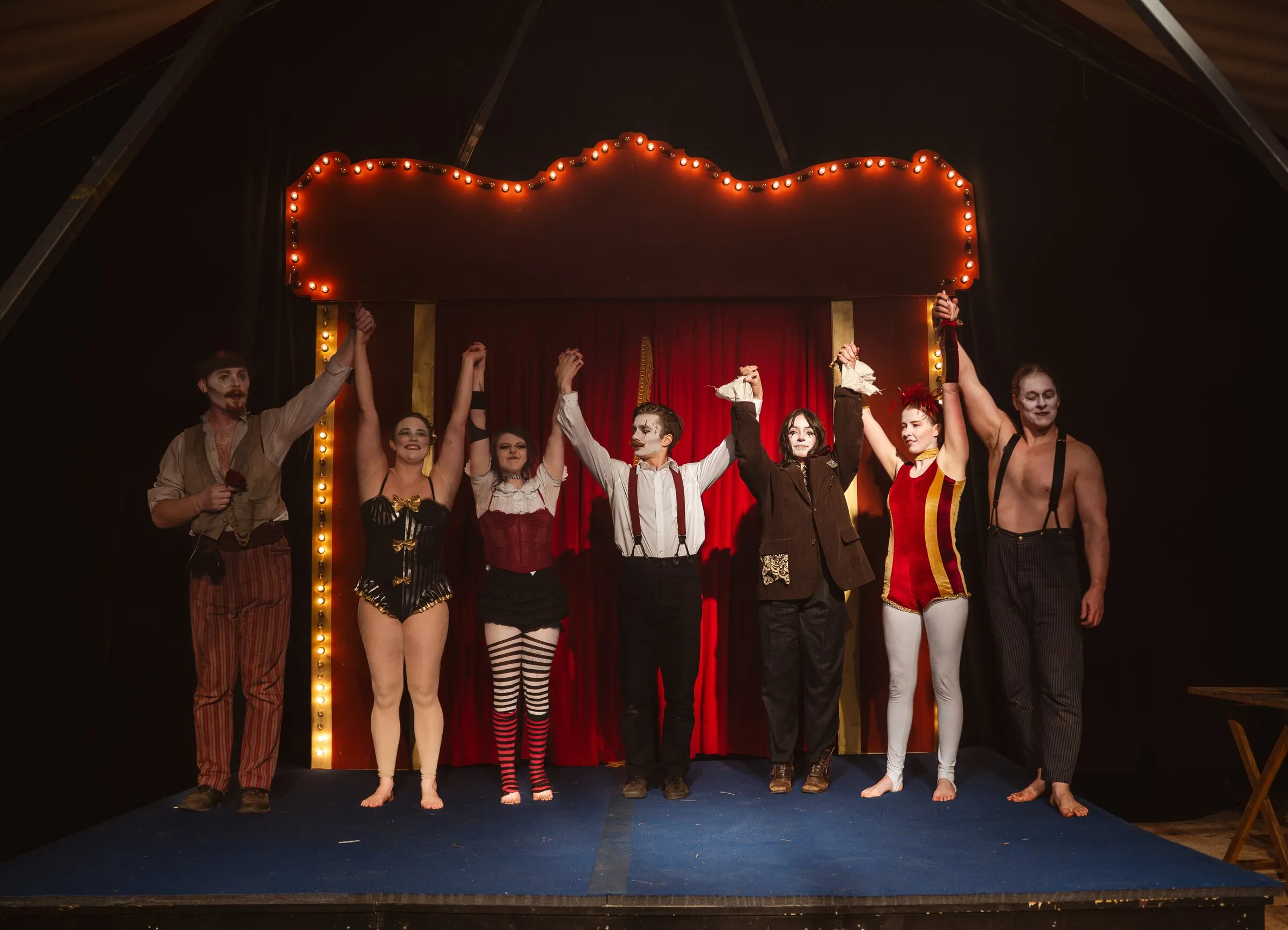 The Kuroneko Circus company joining hands for the curtain call beneath the lit proscenium arch
