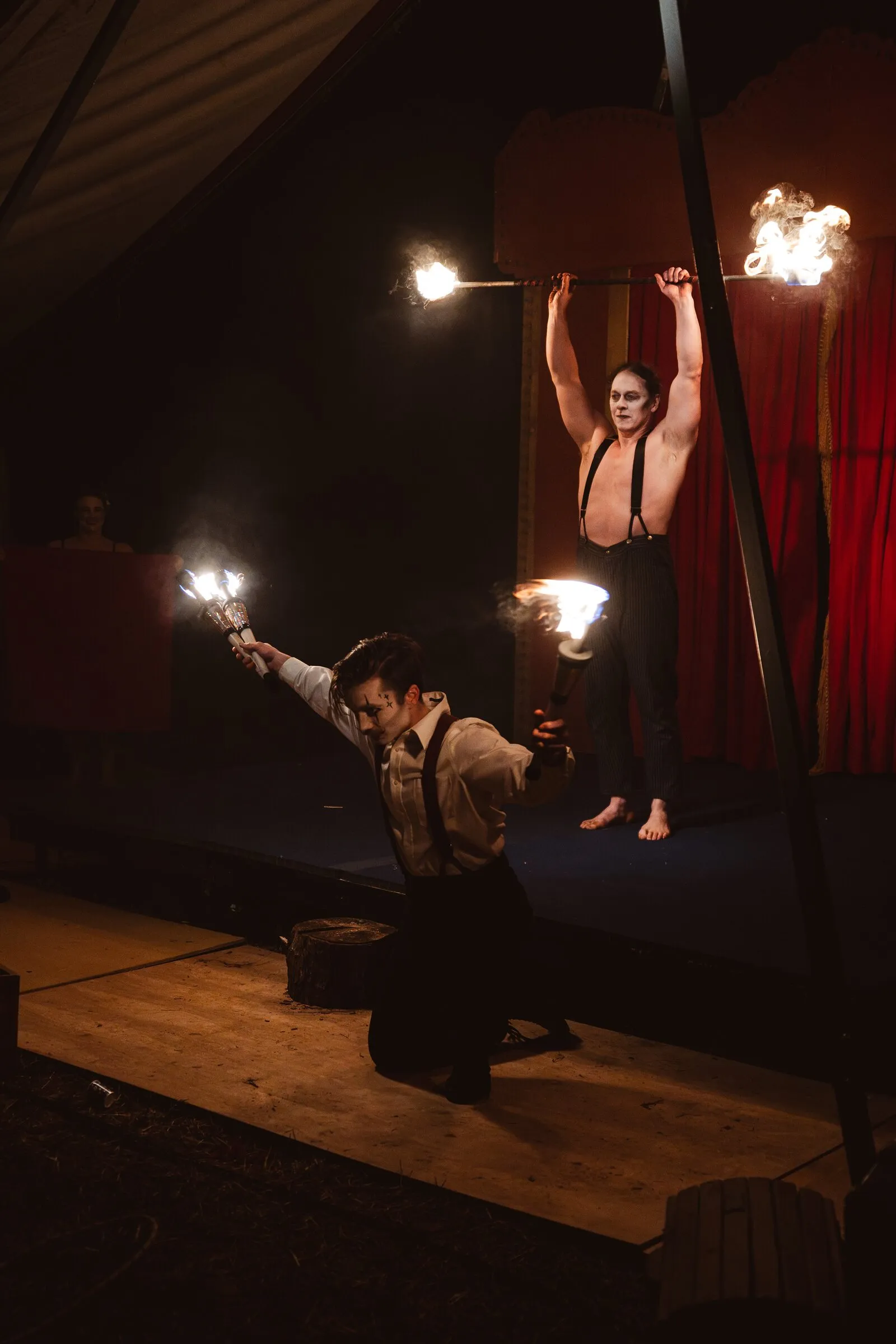 Two Kuroneko Circus fire performers, one kneeling and one standing with torches held overhead
