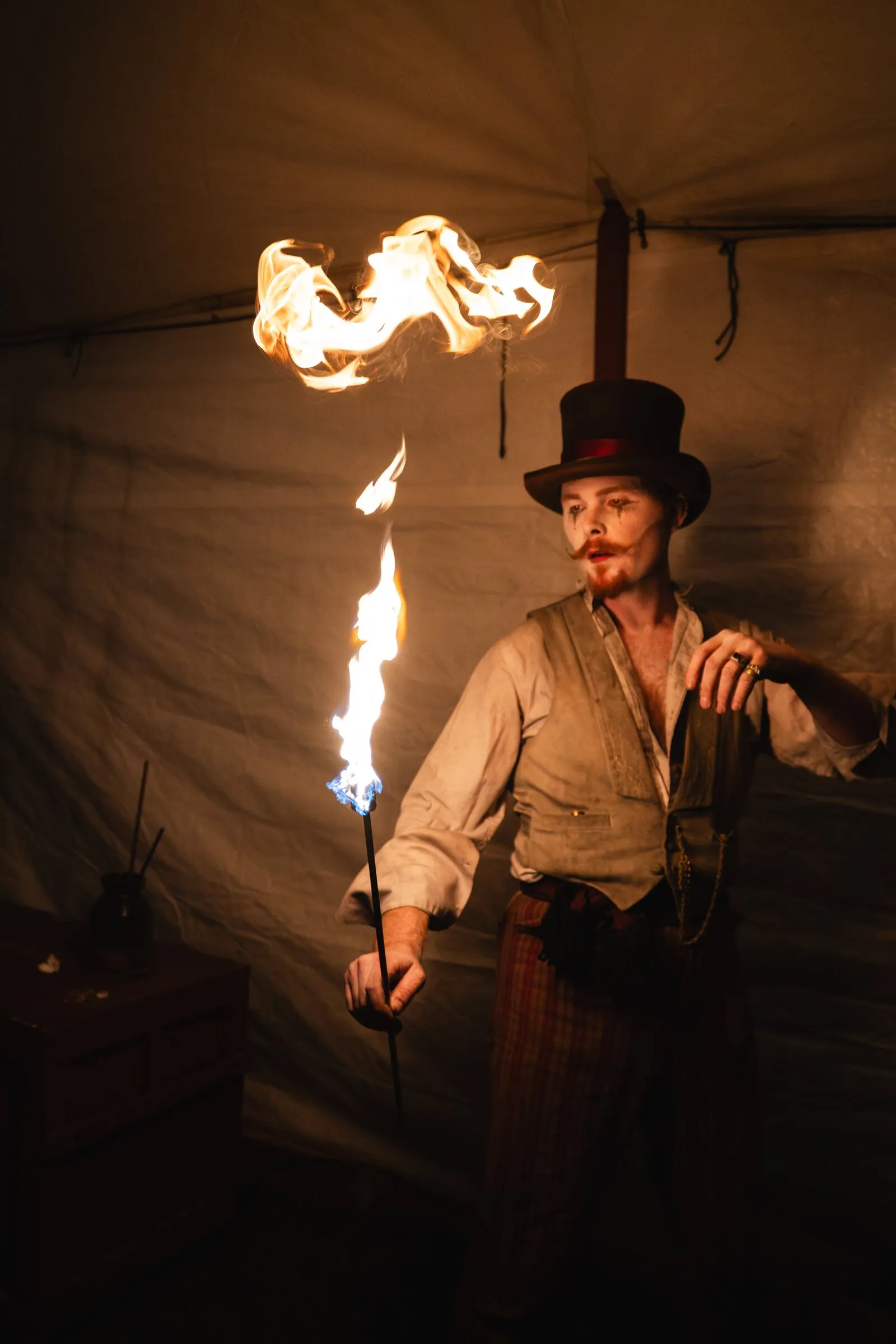 A Kuroneko Circus fire eater in a top hat with a fireball rising beside him