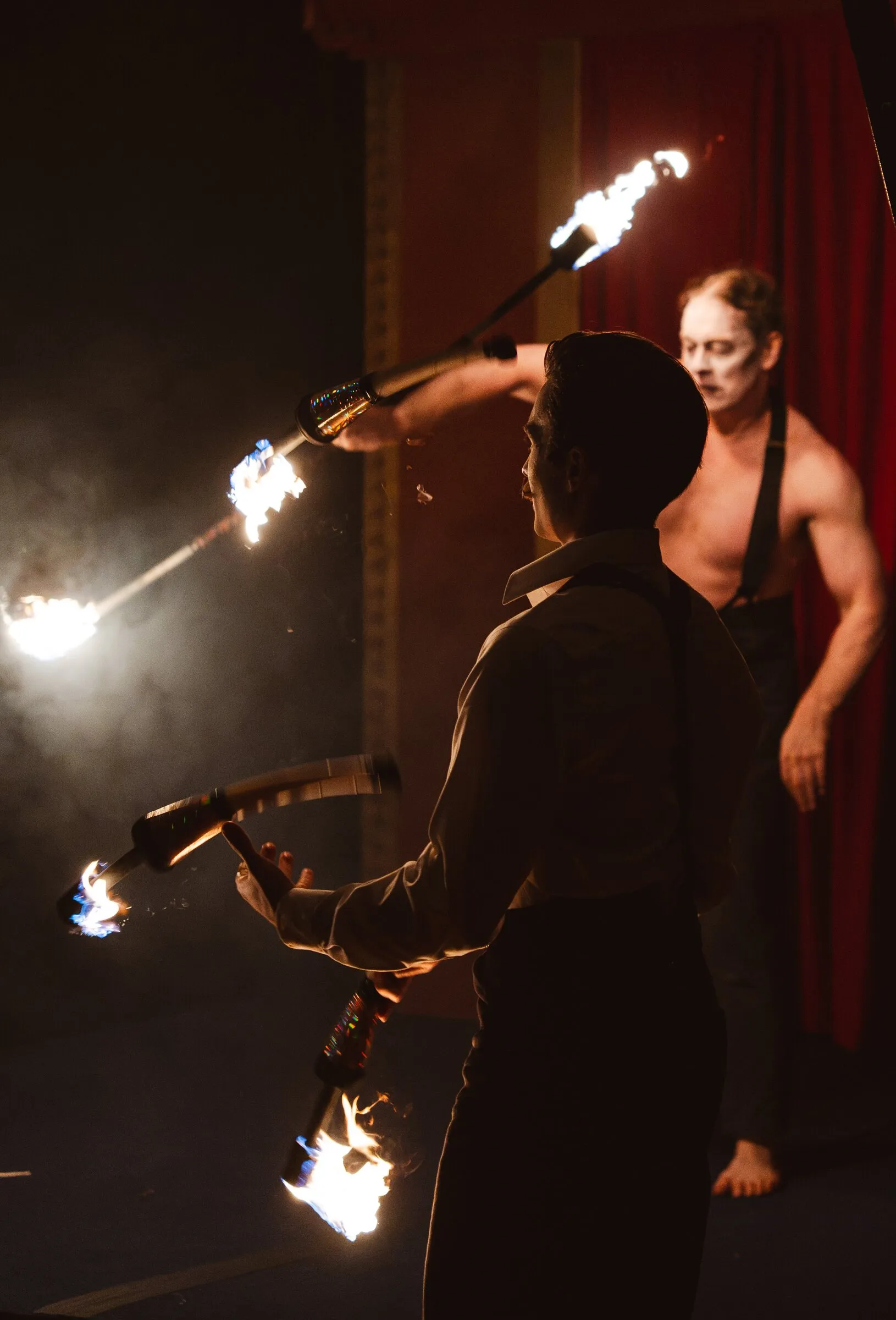 Two Kuroneko Circus performers passing flaming torches between them in the dark