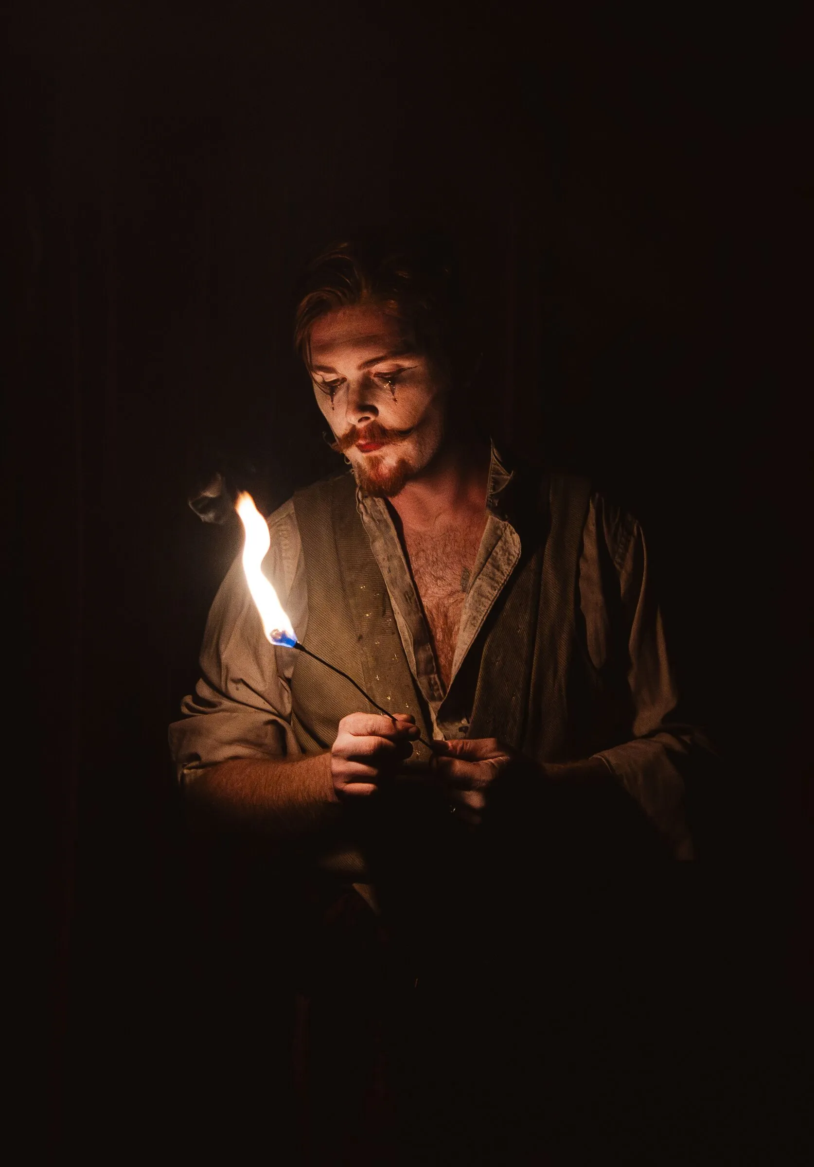 A Kuroneko Circus fire performer lit only by the small flame he holds