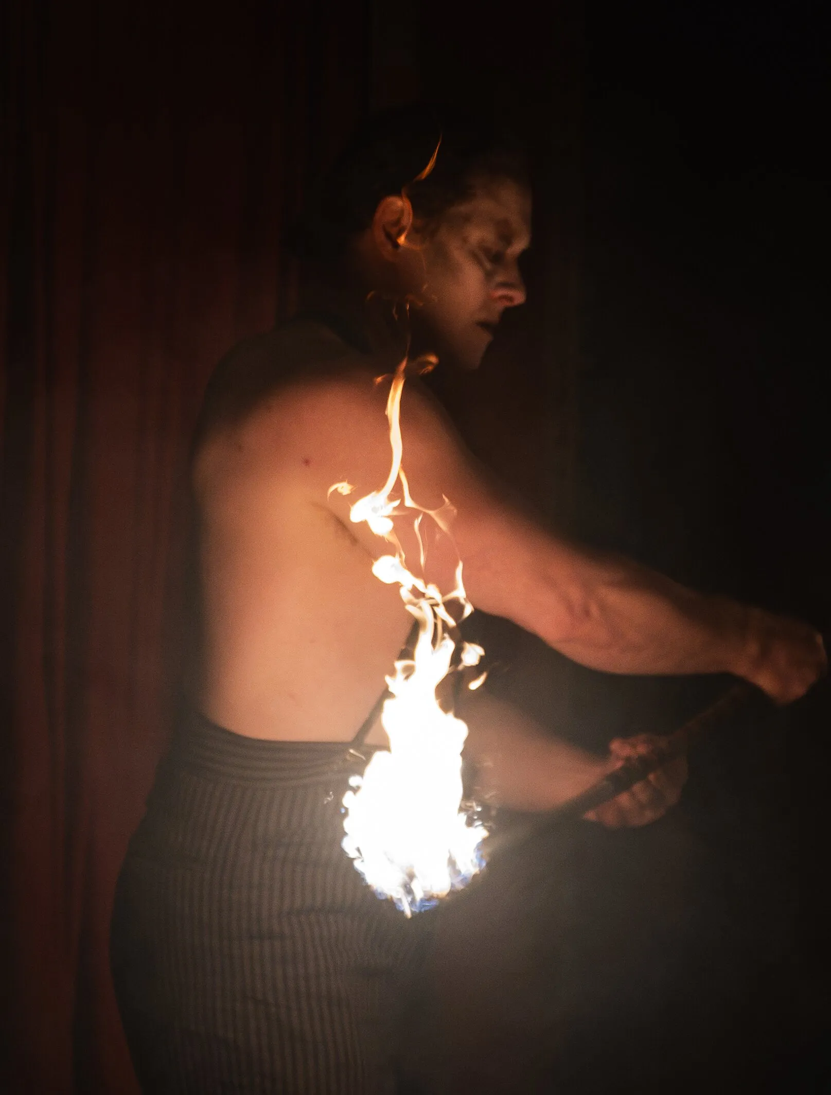 A shirtless Kuroneko Circus fire performer running a flaming torch along his bare skin