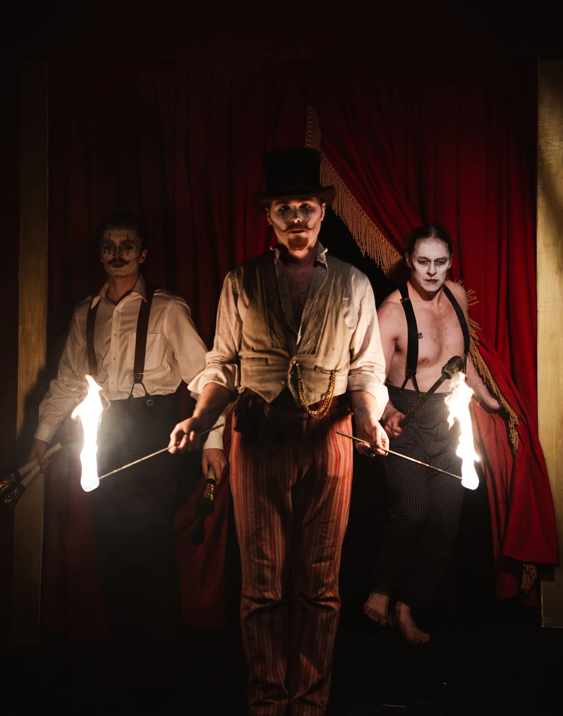 Three Kuroneko Circus fire performers stepping through the curtain holding lit torches