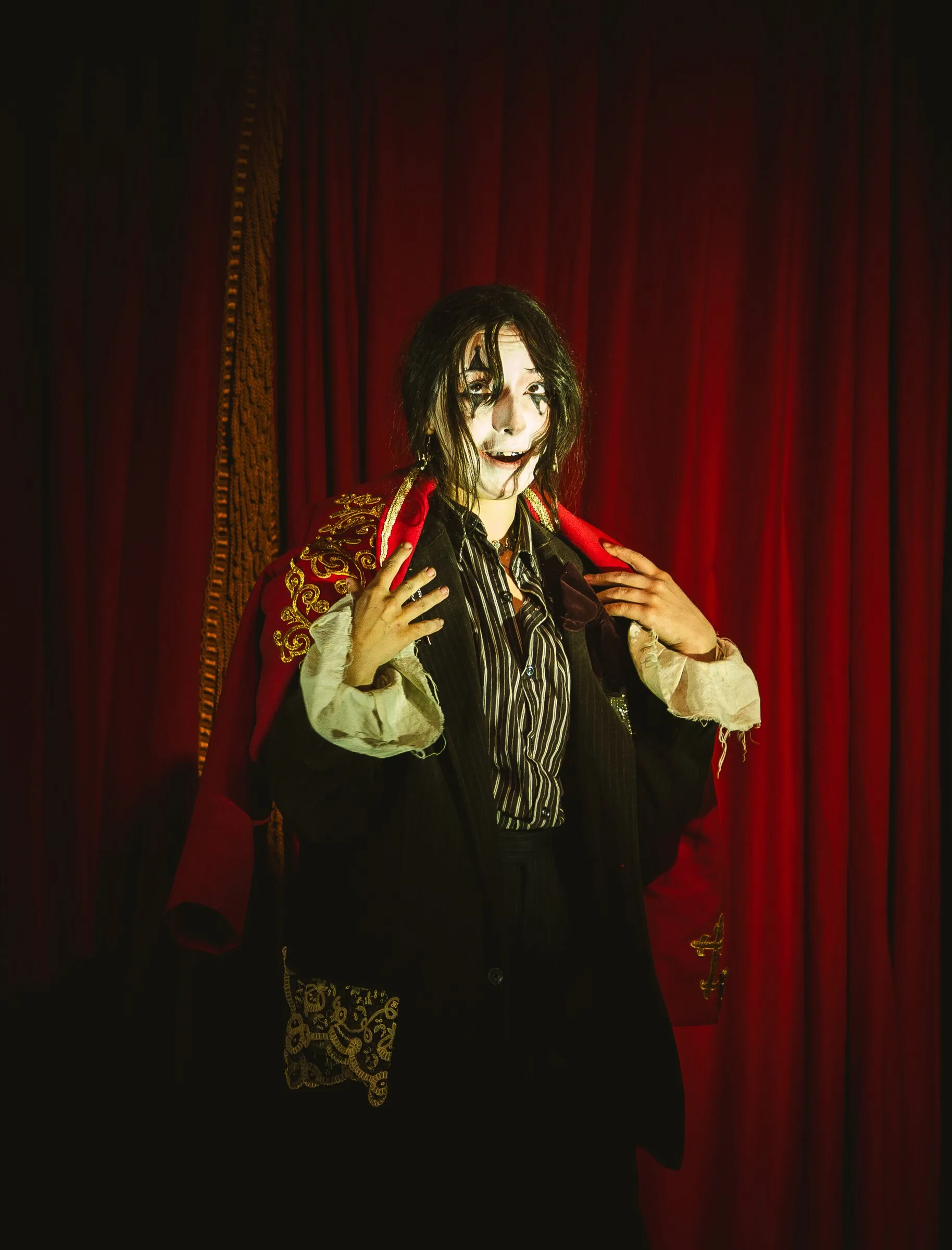 A Kuroneko Circus sideshow character in whiteface and a ruffled collar grinning at the audience